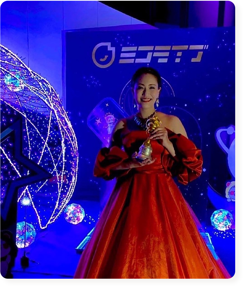 ステージでトロフィーを掲げるドレス姿の女性パフォーマー