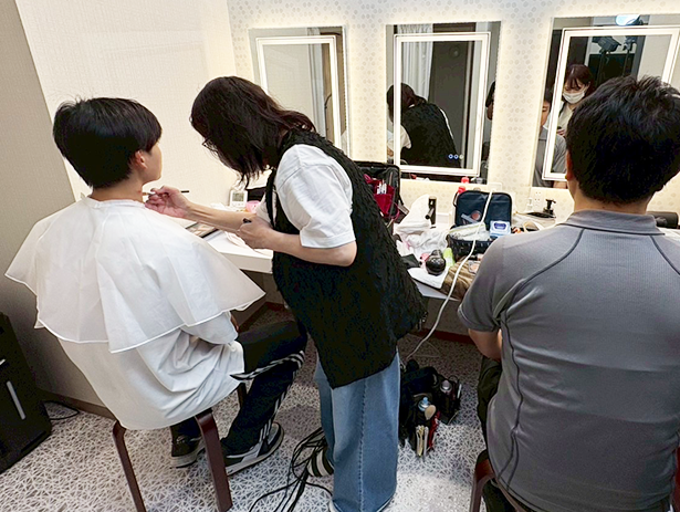 控室でメイクを受ける出演者とスタッフ